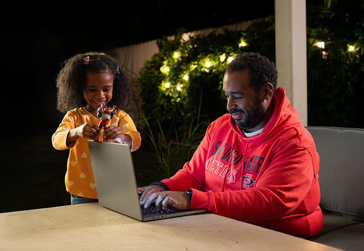 Man typing on a laptop while daughter plays with a toy